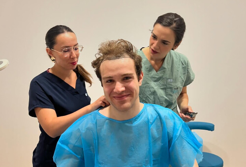 Uomo sorridente durante un trapianto di capelli assistito da due dottoresse